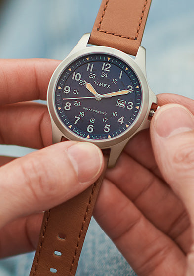 Timex Expedition Field Post Solar watch with a navy dial and silver-tone case shown in hand, with the crown being adjusted.