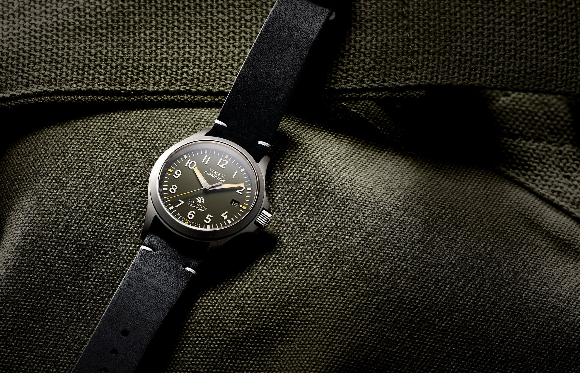 The Timex Expedition Titanium displayed flat on olive-green textured fabric, showcasing its brushed titanium case and classic field watch design.