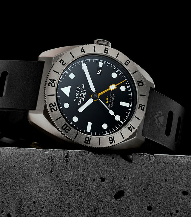 The Timex Expedition North GMT Titanium Automatic displayed against a black background, showcasing its titanium case, black dial, and yellow GMT hand.