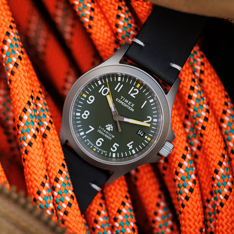 The Timex Expedition Titanium with a green dial and black strap positioned on bright orange climbing rope, emphasizing its rugged outdoor appeal.