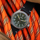 The Timex Expedition Titanium with a green dial and black strap positioned on bright orange climbing rope, emphasizing its rugged outdoor appeal.