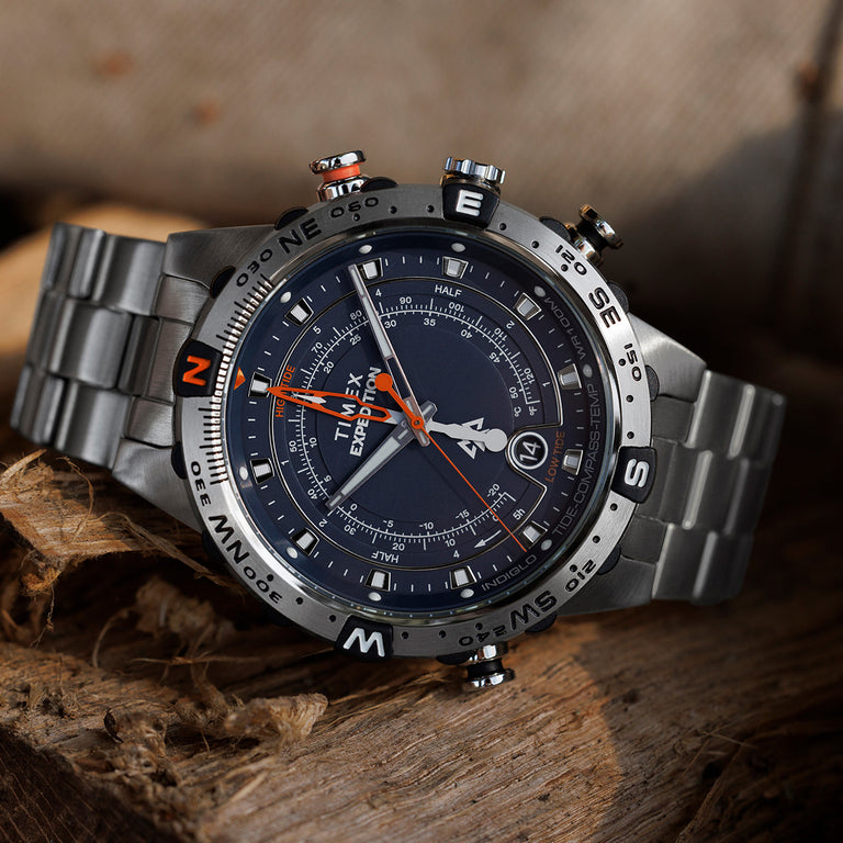 Detailed close-up of the Timex Expedition Tide-Temp-Compass resting on a wooden surface, highlighting the textured dial, compass bezel with cardinal points, and bold orange hands.