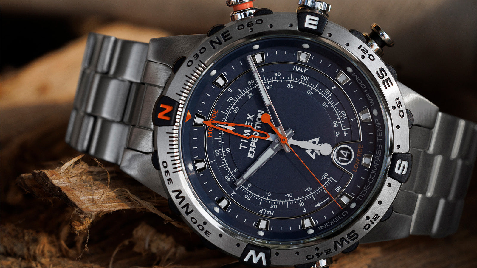 Extreme close-up of the watch face of the Timex Expedition Tide-Temp-Compass, showing the intricate dial details, bold compass bezel with N, E, S, W markings, and bright orange tide hand.