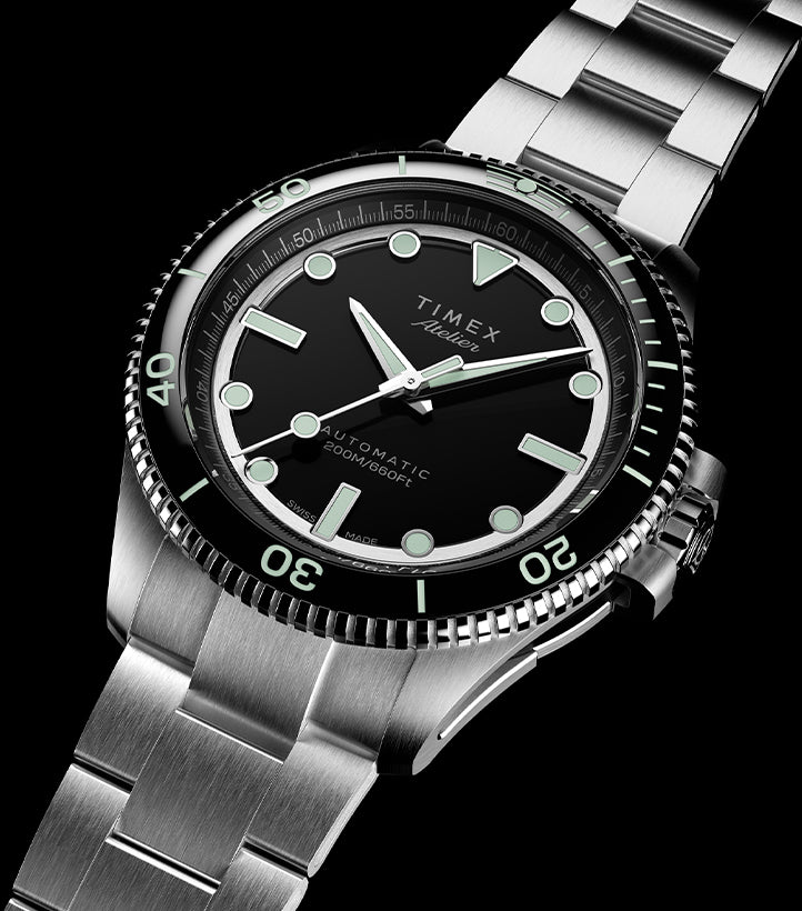 Angled front view of the Timex Atelier automatic dive watch with a stainless steel bracelet, black dial, luminous indices, and rotating bezel with 200M water resistance marking.