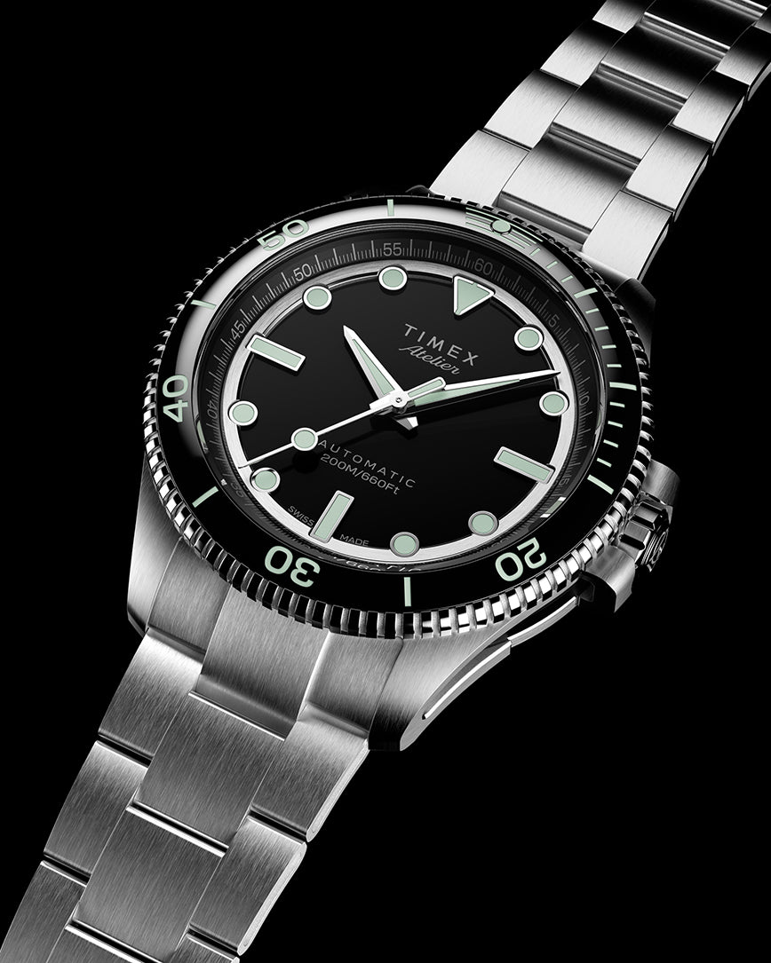 Angled front view of the Timex Atelier automatic dive watch with a stainless steel bracelet, black dial, luminous indices, and rotating bezel with 200M water resistance marking.