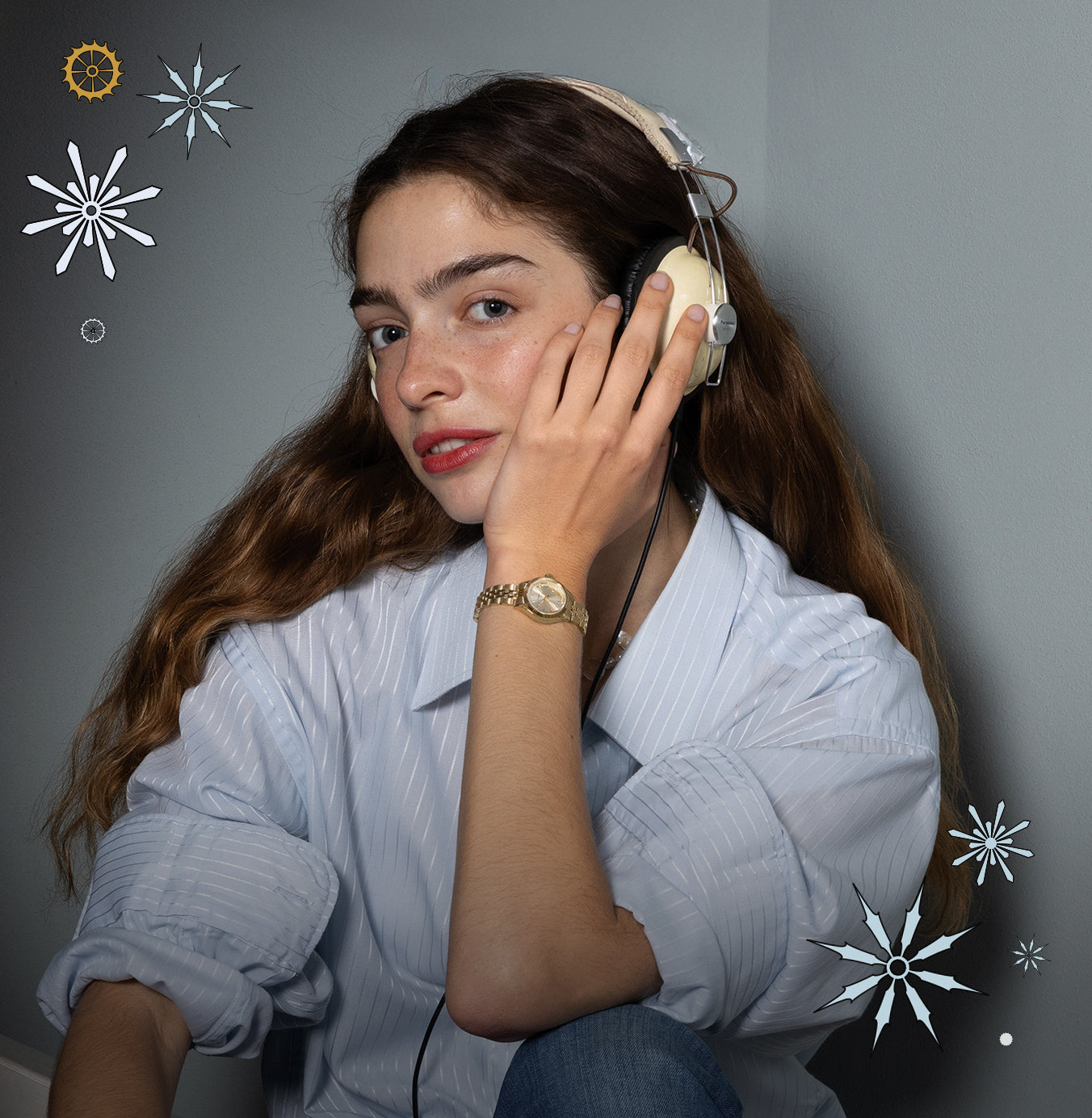 A woman wearing a light blue striped shirt and headphones smiles softly while showing her gold Timex watch, surrounded by illustrated snowflakes on a gray background.