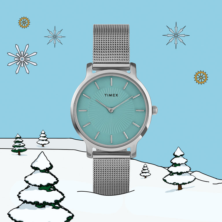 Timex women’s watch with a turquoise sunray dial and silver mesh strap set against a snowy illustrated background with pine trees and snowflakes.