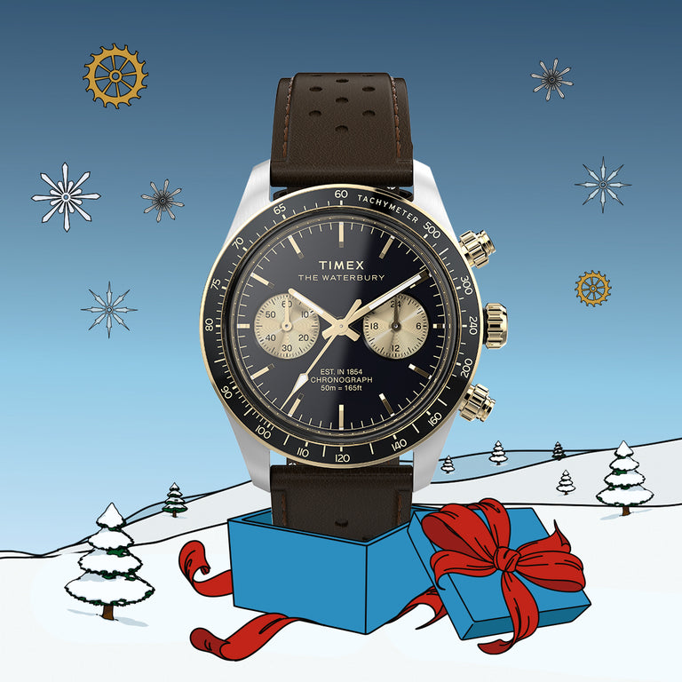 Timex Waterbury Chronograph with a black dial and brown leather strap displayed in a blue gift box on a snowy illustrated landscape with trees and snowflakes.