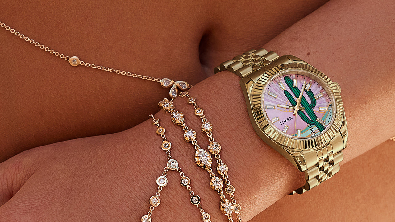 Lifestyle image of a woman wearing the Timex x Jacquie Aiche “Desert Daze” gold-tone watch with diamond and gold chain bracelets. The cactus dial glows in the sunlight, evoking bohemian luxury and desert serenity.