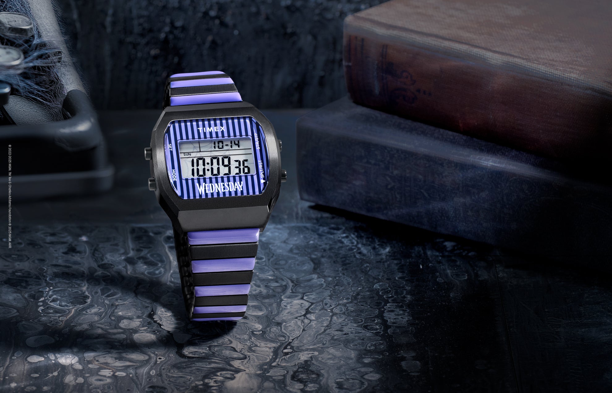 Timex x Wednesday T80 digital watch featuring a black and purple striped design on the face and bracelet. The watch is displayed on a dark, moody surface beside vintage books, evoking a gothic aesthetic inspired by Wednesday Addams.