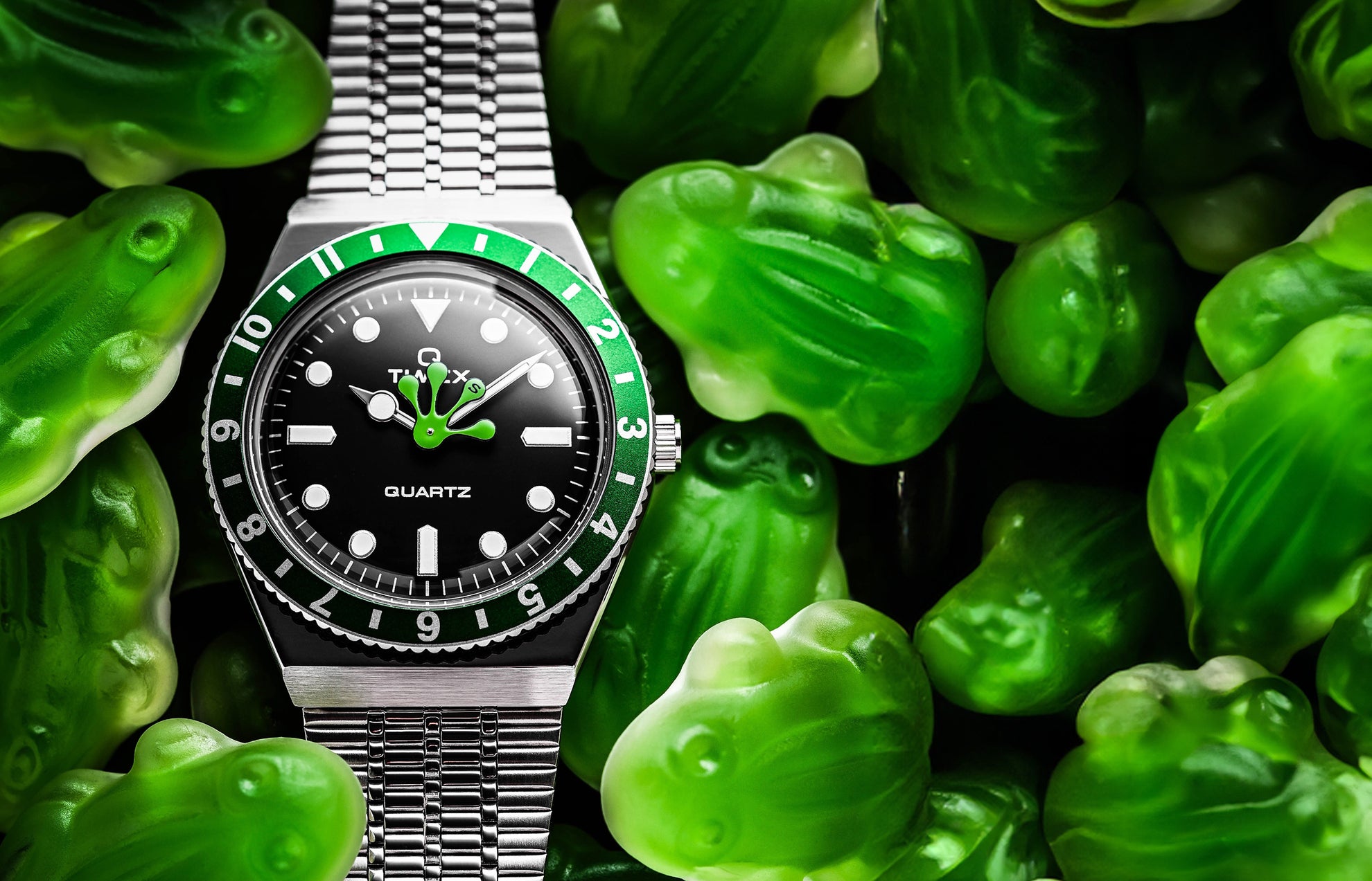 Timex x seconde/seconde/ Q Timex watch with a black dial and green accents surrounded by green gummy frog candies. The hour hand is playfully shaped like a frog’s foot, blending humor and design creativity in seconde/seconde/’s signature style.
