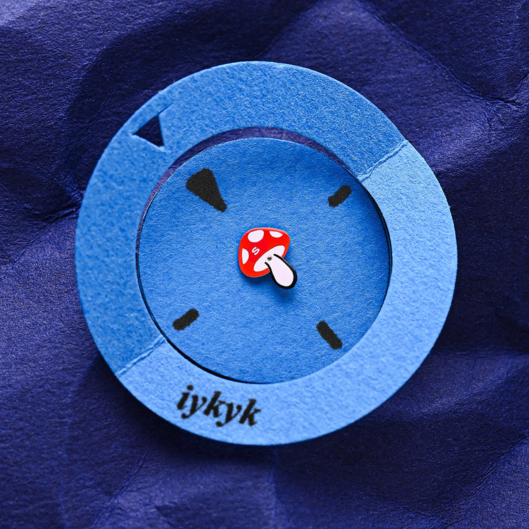 A paper art version of the Q Timex watch face, with a blue circular cutout and a red mushroom seconds hand on a deep blue textured background, featuring the word “iykyk.”