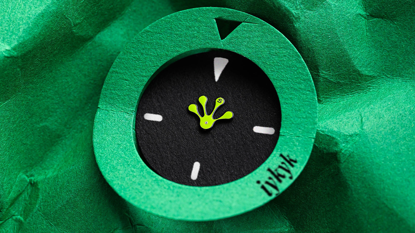 Macro image of the Timex x seconde/seconde/ collaboration showing a green paper cutout watch face with frog foot-shaped hand on a textured green background, highlighting the conceptual artistry of the design.