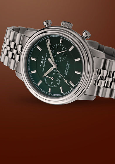 Timex Waterbury Metropolitan Chronograph watch featuring deep green dial, chronograph sub-dials, and polished stainless steel bracelet on a brown backdrop.