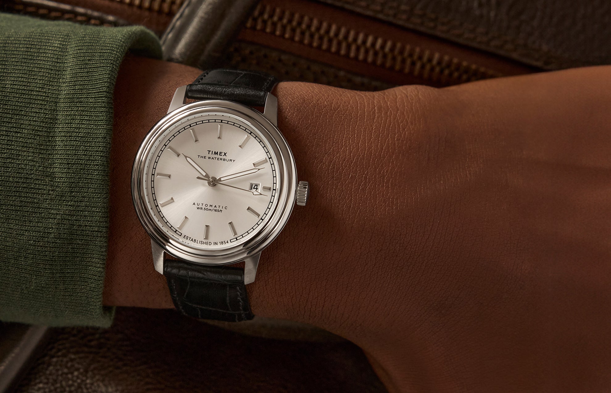 Timex Waterbury Metropolitan Automatic watch on wrist, featuring a minimalist silver dial, stainless steel case, and black leather strap with croc texture.