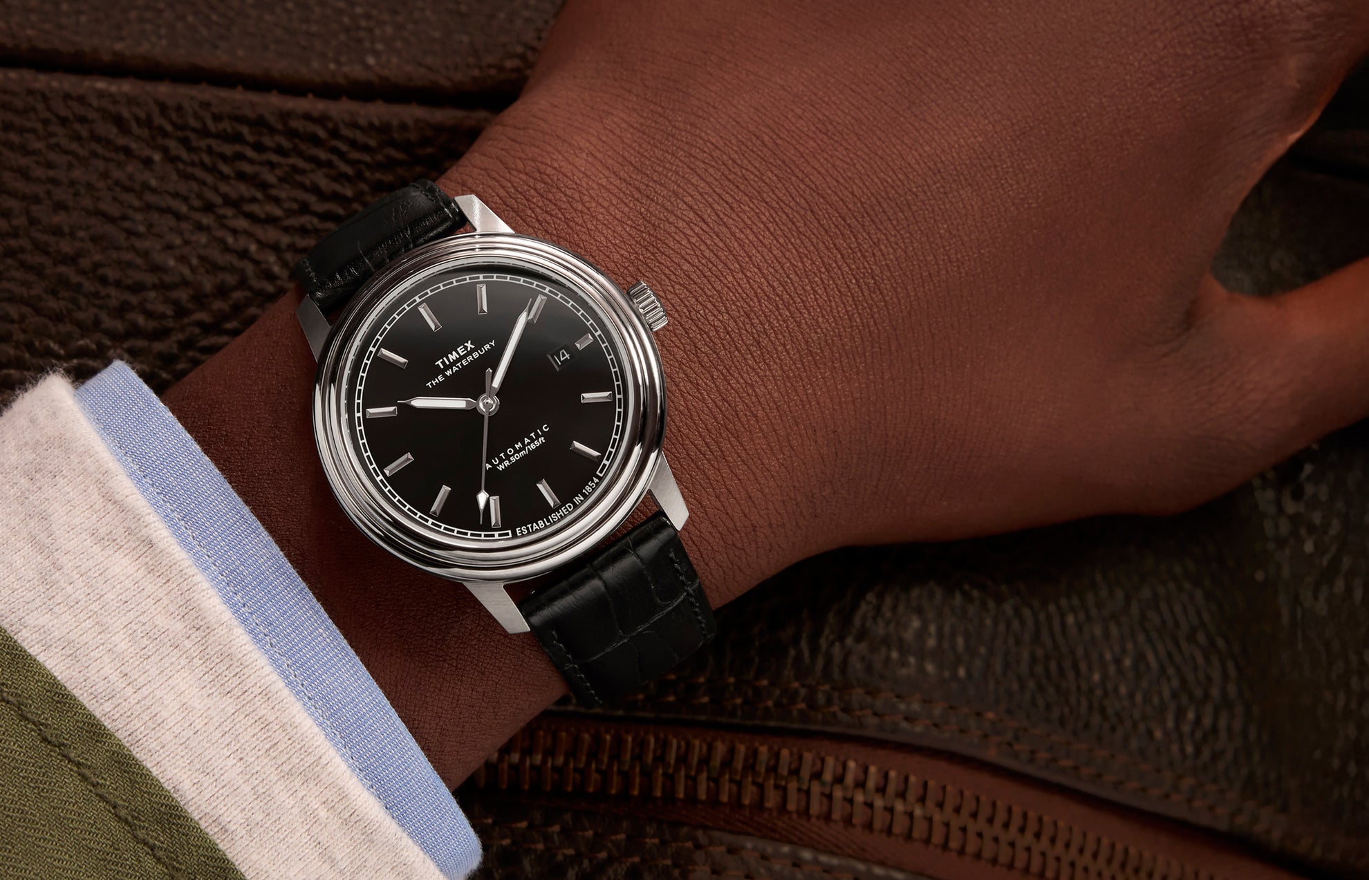 Timex Waterbury Metropolitan Automatic watch on wrist, paired with a dress shirt and jacket, showcasing the sleek black dial and classic leather strap.