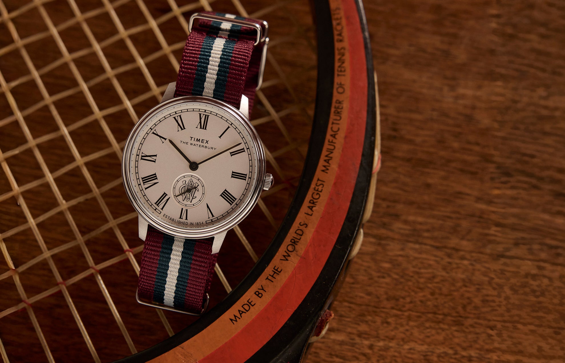 Timex Waterbury Metropolitan Sub-Second with white dial and red, white, and blue-striped fabric strap placed on a vintage wooden tennis racket.