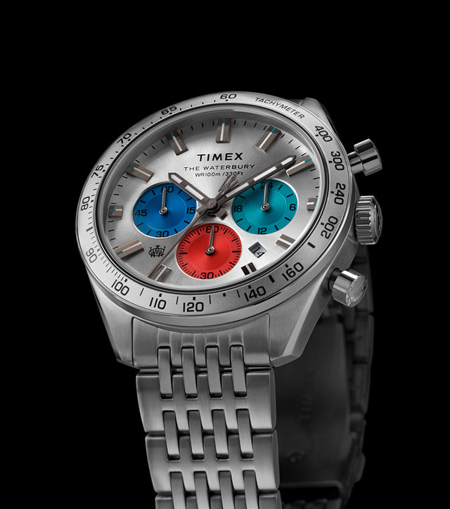 Timex Waterbury Chronograph with silver case, tachymeter bezel, and tricolor chronograph sub-dials against a black background.