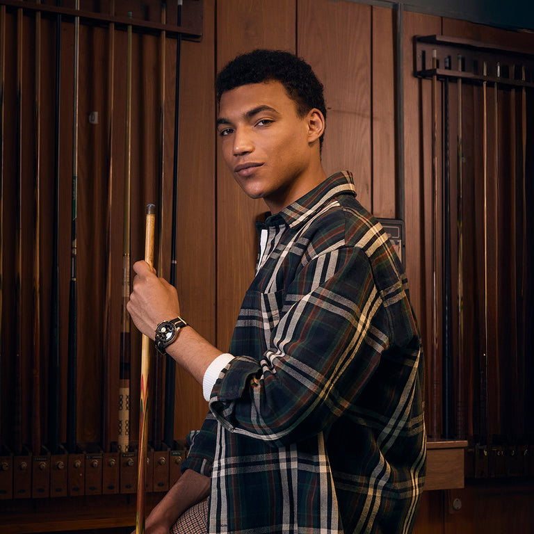 Man wearing the Timex Waterbury Heritage Chronograph with black and gold dial while holding a pool cue in a billiards room.