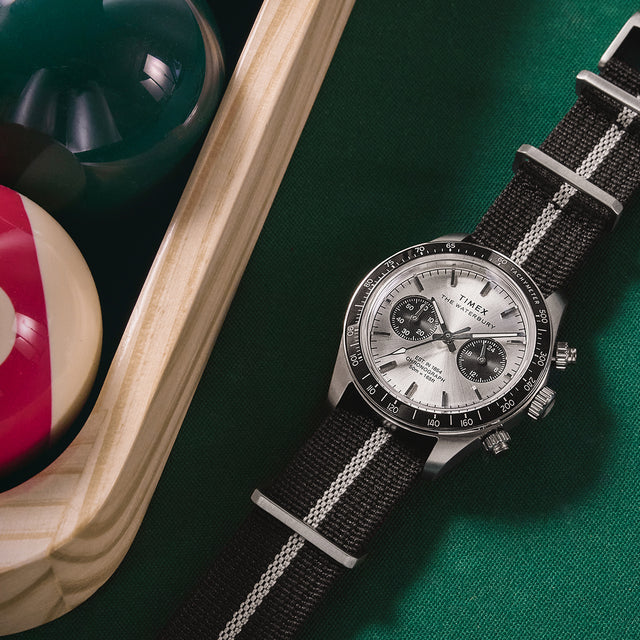 Timex Waterbury Heritage Chronograph positioned beside billiard balls, showcasing its silver dial, black sub-dials, and sporty design.