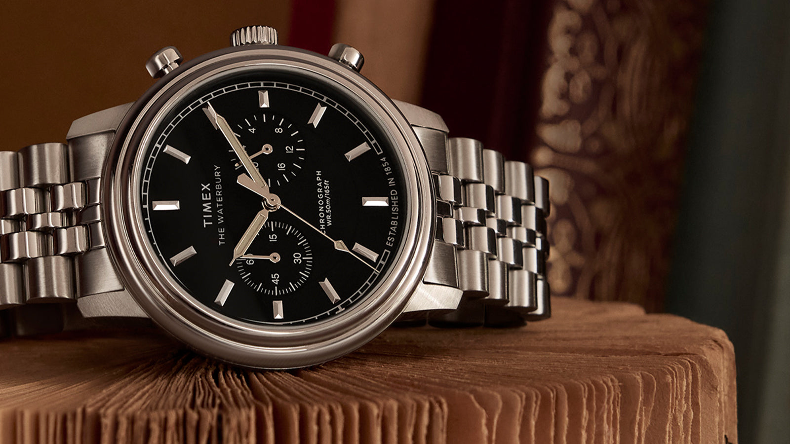 Timex Waterbury Metropolitan Chronograph with black dial and stainless steel bracelet resting on an open vintage book, showcasing its polished finish and sub-dials.