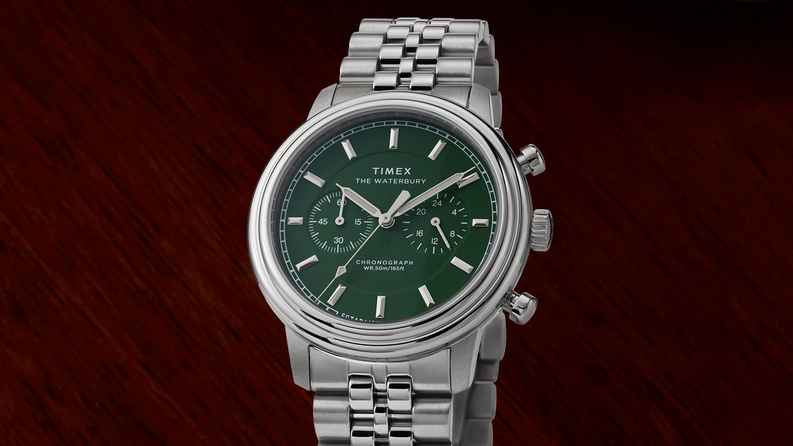 Front-facing image of the Timex Waterbury Metropolitan Chronograph with stainless steel bracelet and green dial on dark wood surface.