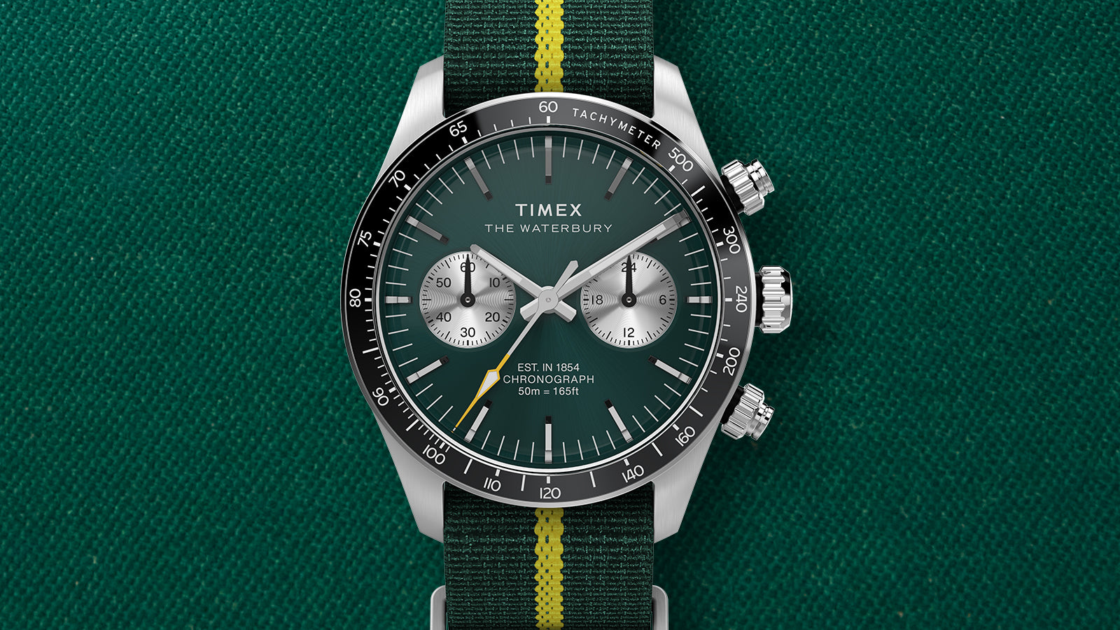 Close-up of the Timex Waterbury Heritage Chronograph showing green dial, black tachymeter bezel, and yellow-accented second hand.
