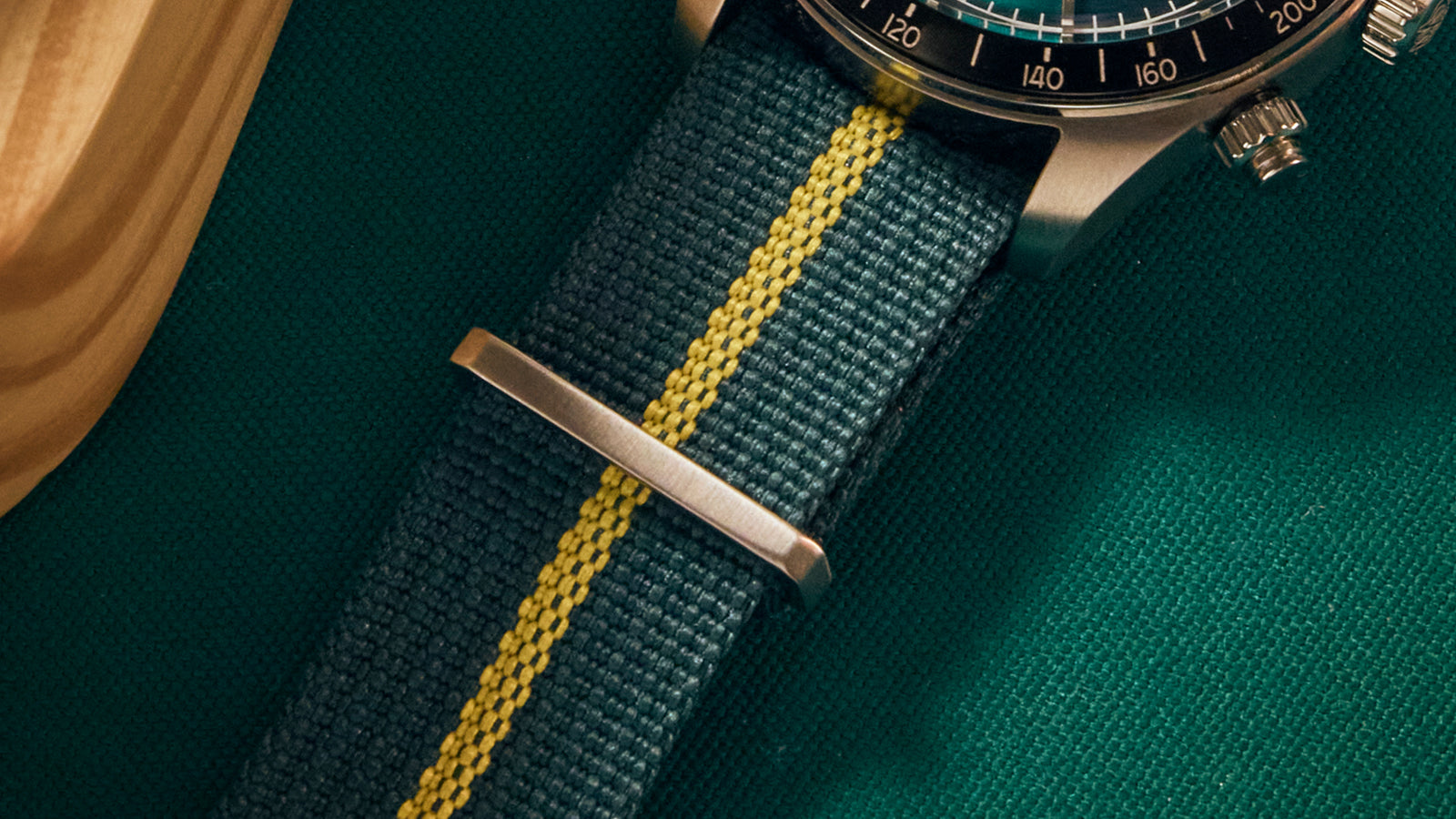 Close-up of the Timex Waterbury Heritage Chronograph’s green fabric strap with a yellow center stripe and stainless-steel hardware.