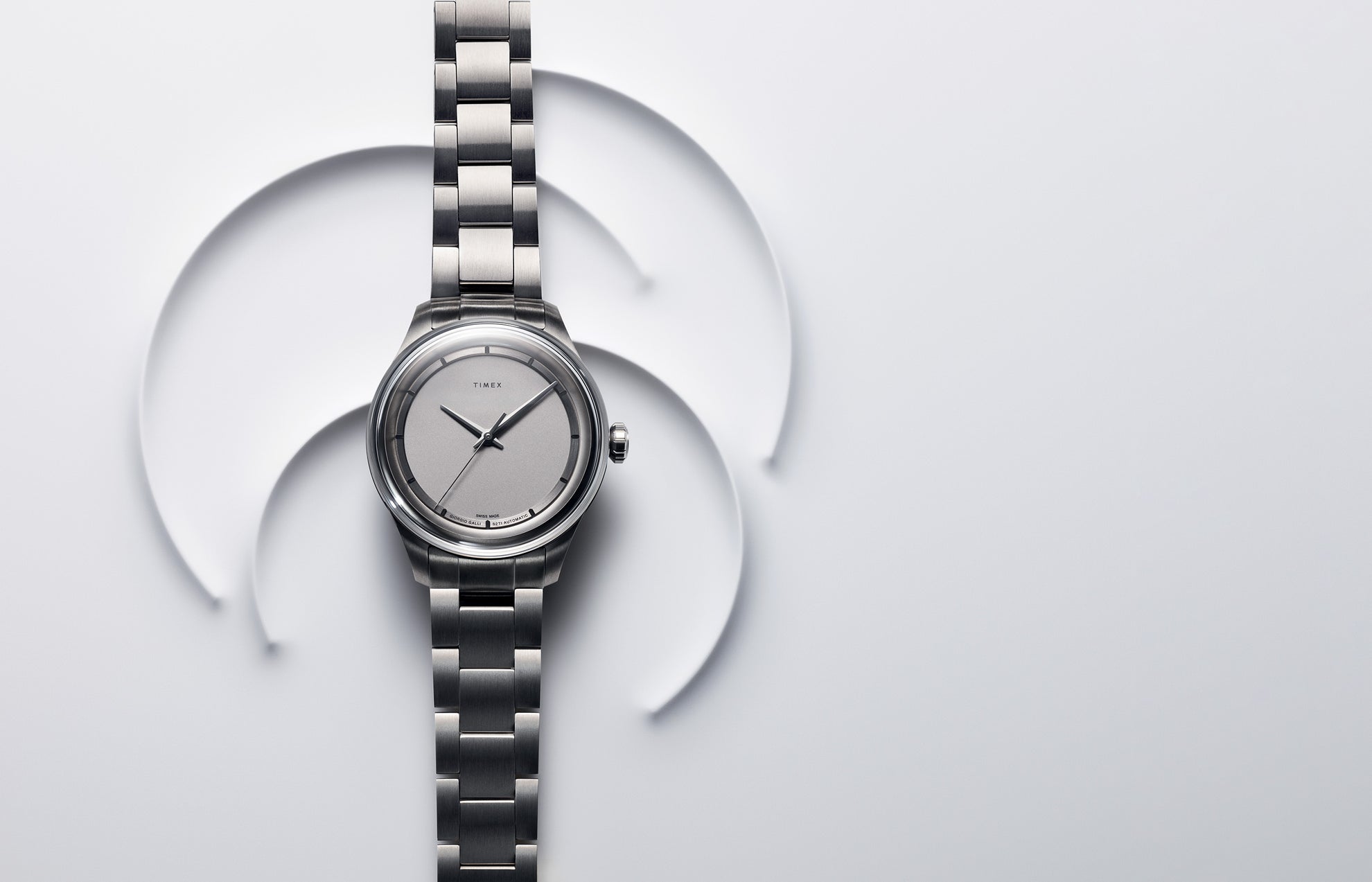Timex Giorgio Galli S2Ti Swiss Made Automatic watch with a titanium case and silver dial, displayed on a minimalist white background with abstract circular shapes.