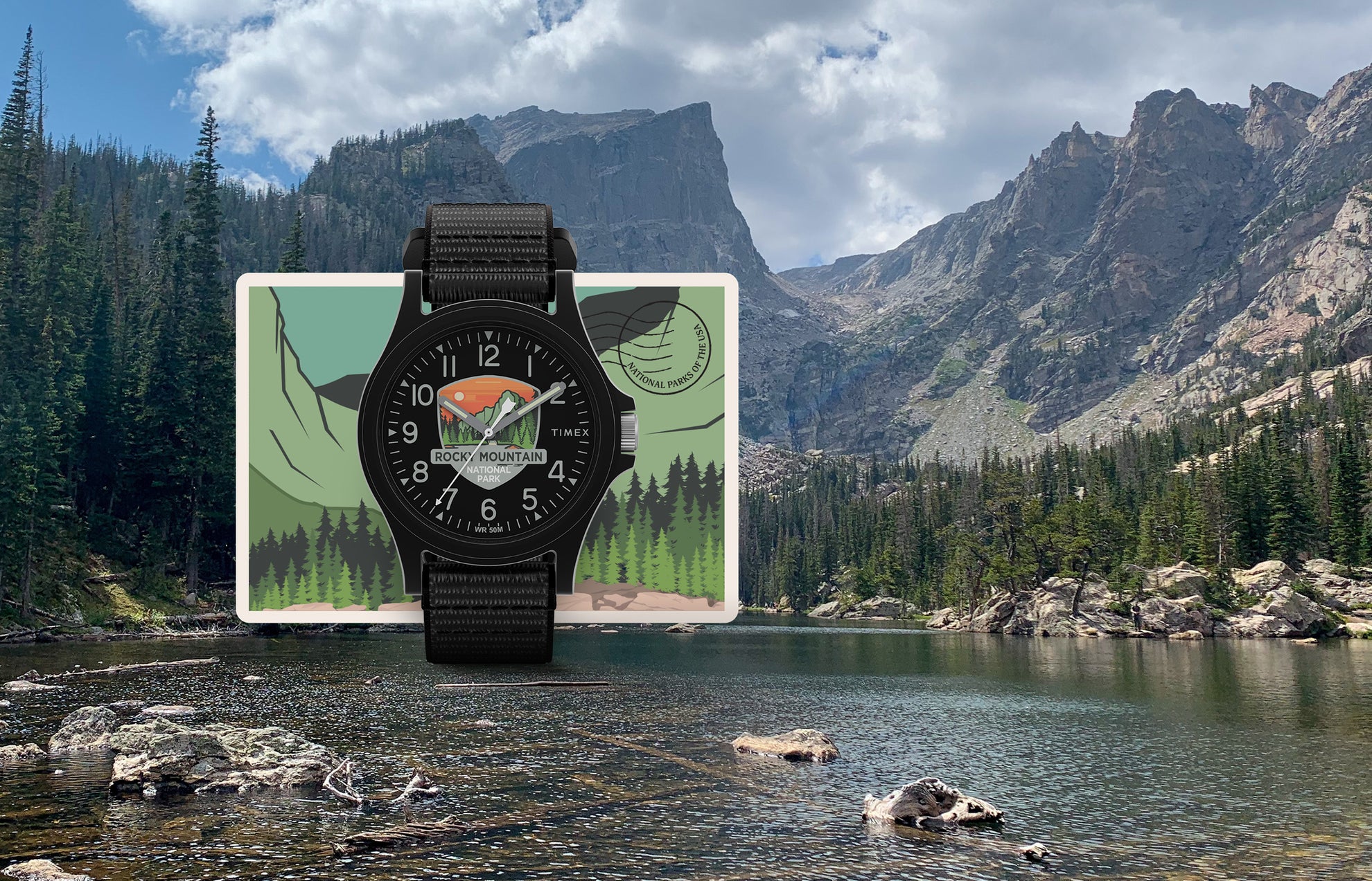 Timex Rocky Mountain National Park watch with a black case and strap, featuring a scenic mountain and forest dial design, displayed over a postcard-style background of a mountain lake.
