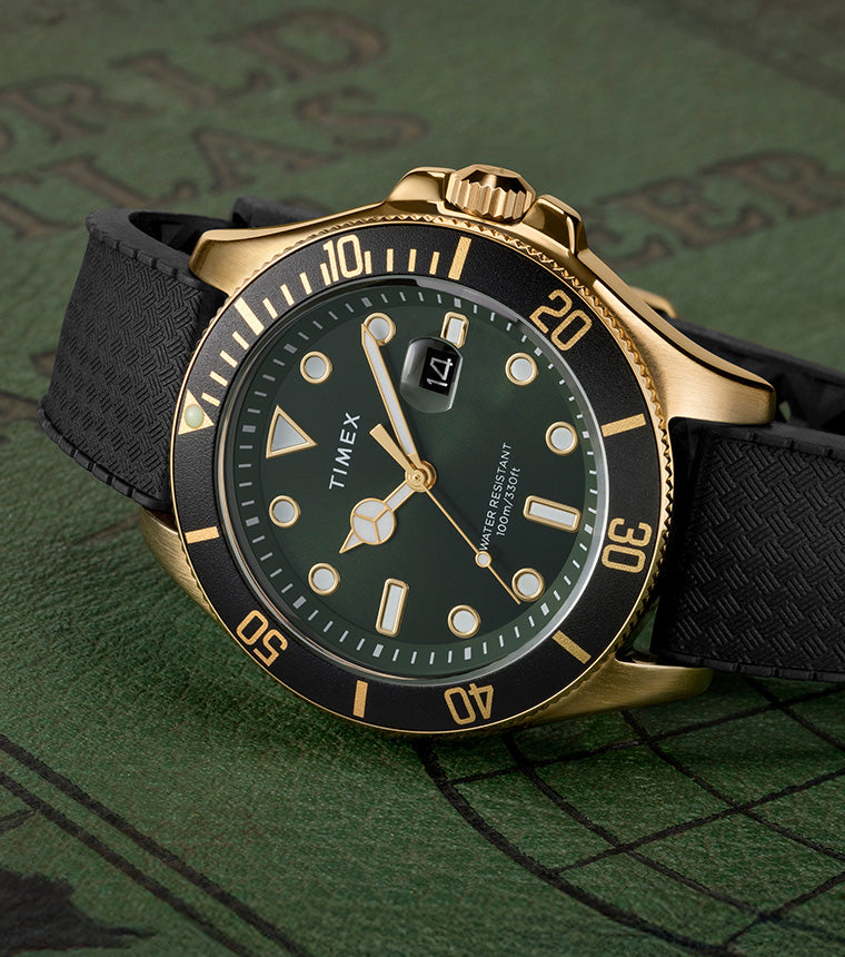 Timex Harborside Coast watch with a green dial, black bezel, and gold-tone stainless-steel case on a textured black strap, displayed on a vintage green world map background.