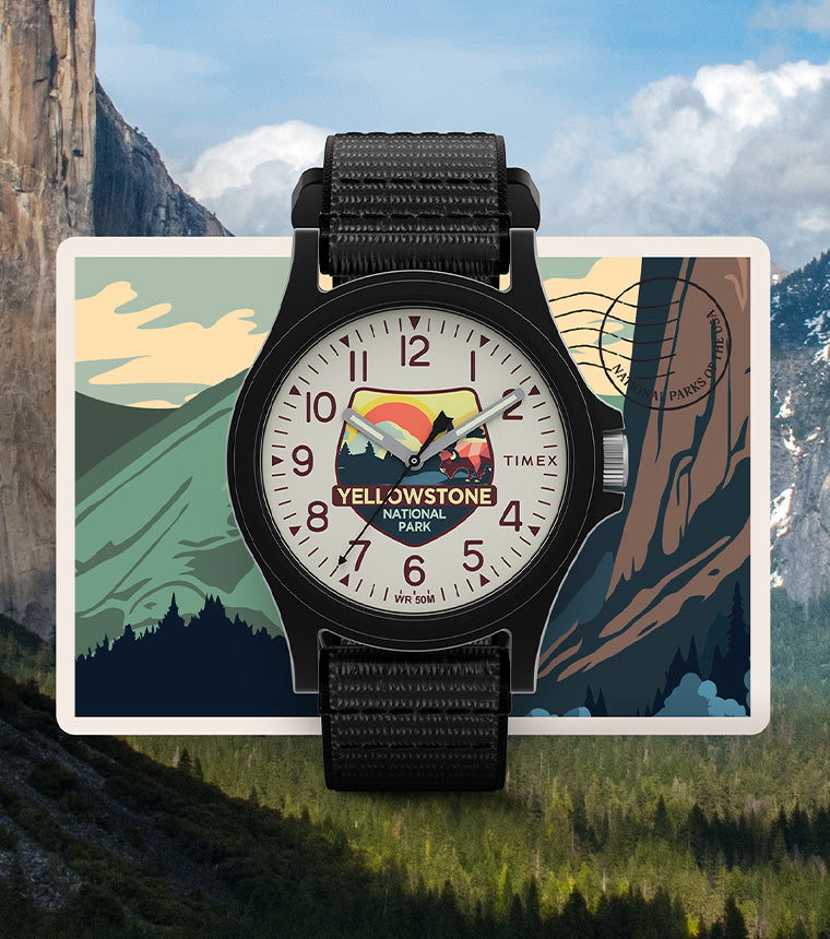 Timex Yellowstone National Park watch with black case and strap, featuring a colorful mountain and bison dial design, displayed over a postcard-style background with cliffs and waterfalls.