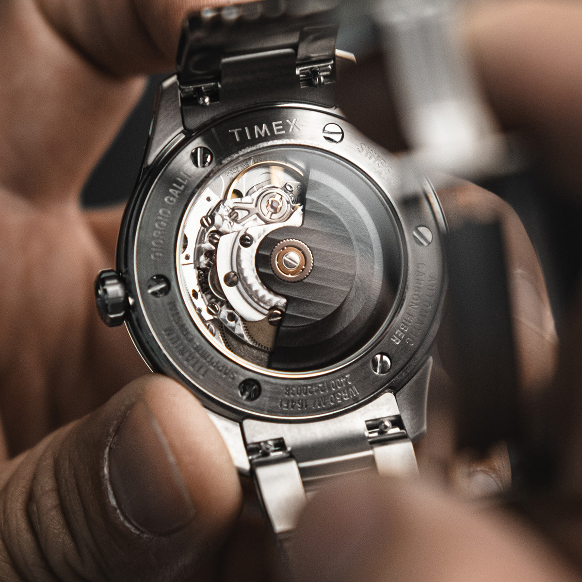 Macro shot of the automatic movement visible through the exhibition back of the Timex Giorgio Galli S2Ti watch, held gently in hand.