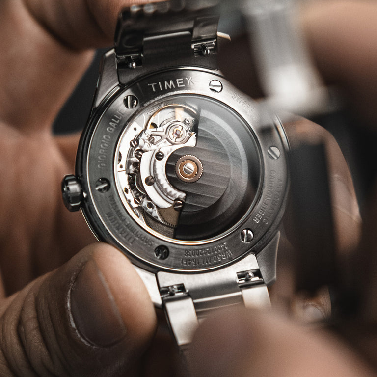 Macro shot of the automatic movement visible through the exhibition back of the Timex Giorgio Galli S2Ti watch, held gently in hand.