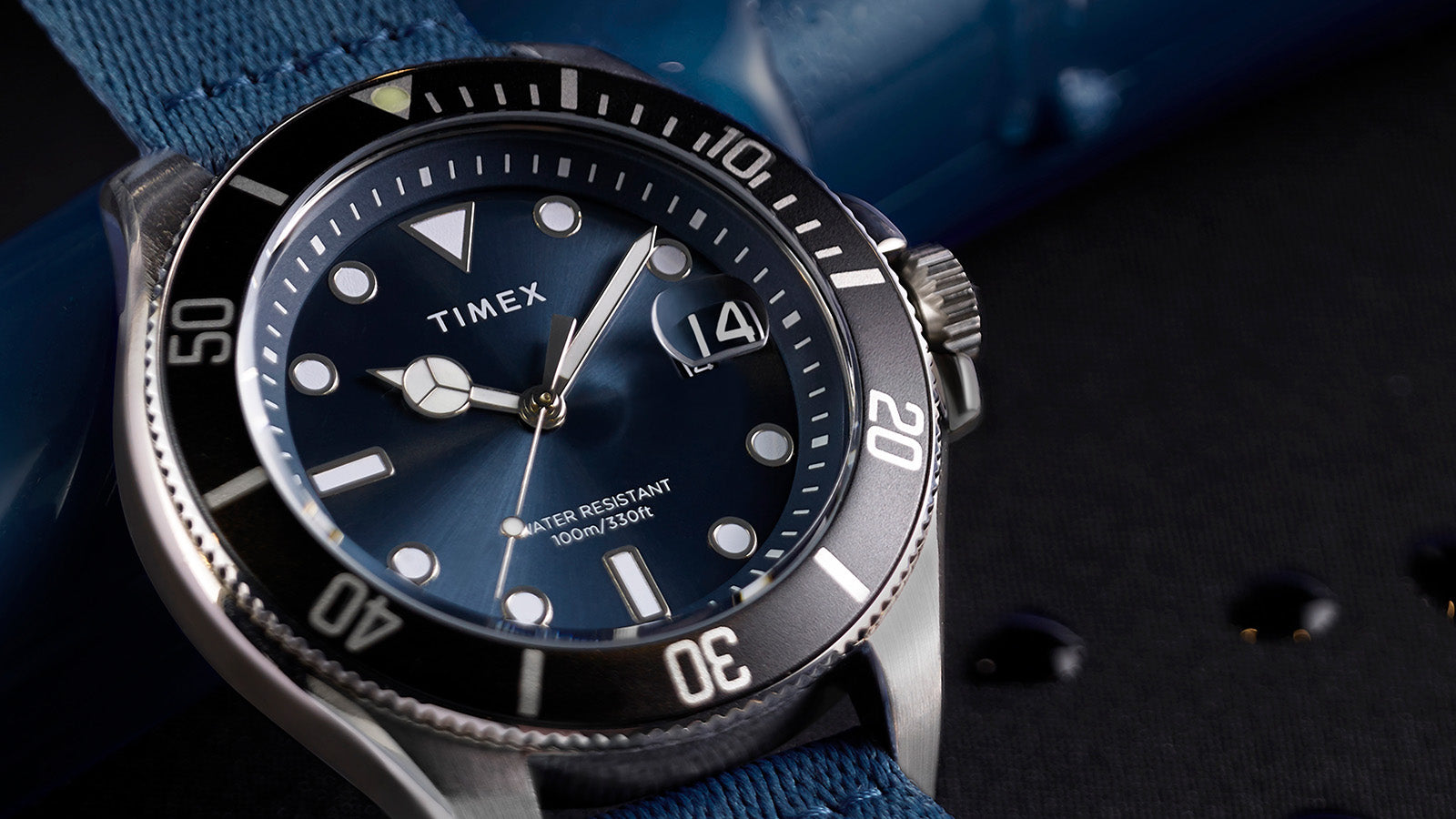 Close-up of the TIMEX® Harborside Coast watch face featuring a blue dial, luminous markers, and a magnified date window at 3 o’clock.