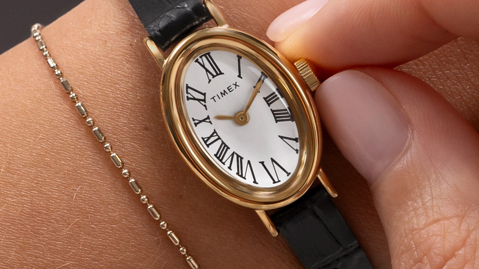 Close-up of a person adjusting the crown of the TIMEX® Cavatina watch on wrist, highlighting its gold-tone case and Roman numeral dial.