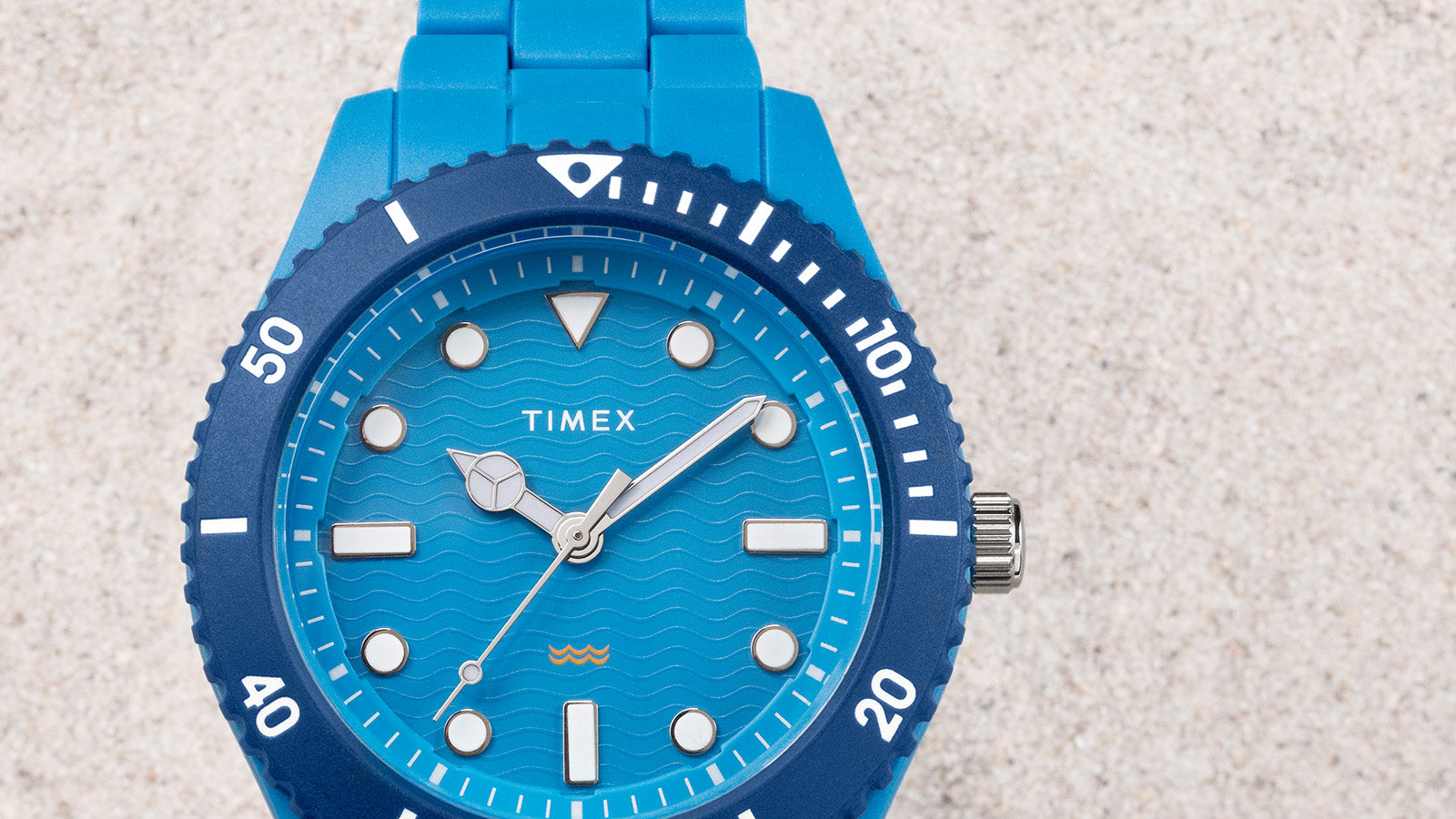 Close-up of the TIMEX® Legacy Ocean #tide watch dial showing wave texture, luminous markers, and a small yellow wave logo.