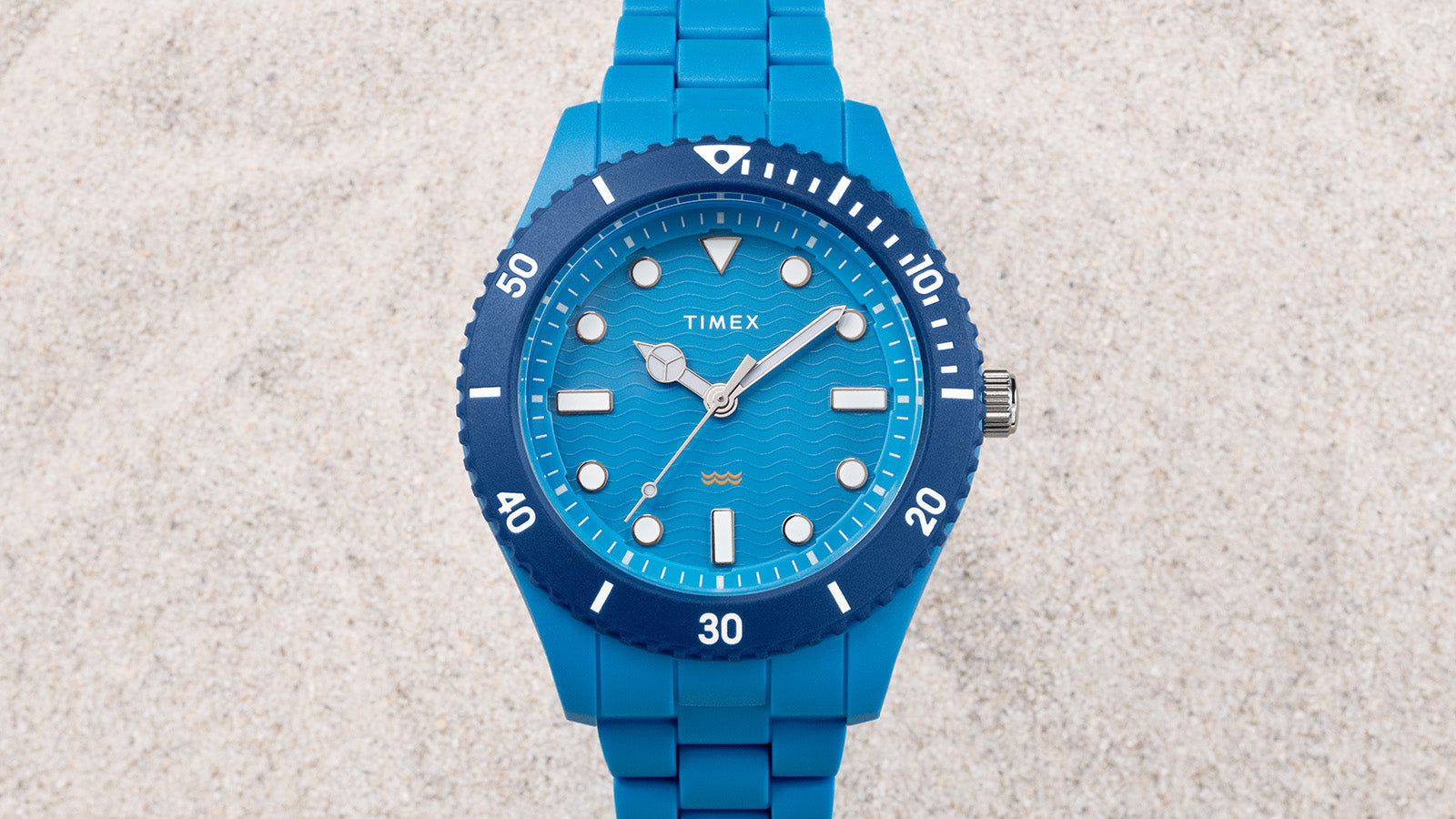 Top-down view of the TIMEX® Legacy Ocean #tide watch in blue with matching bracelet and bezel, displayed on a sandy background.