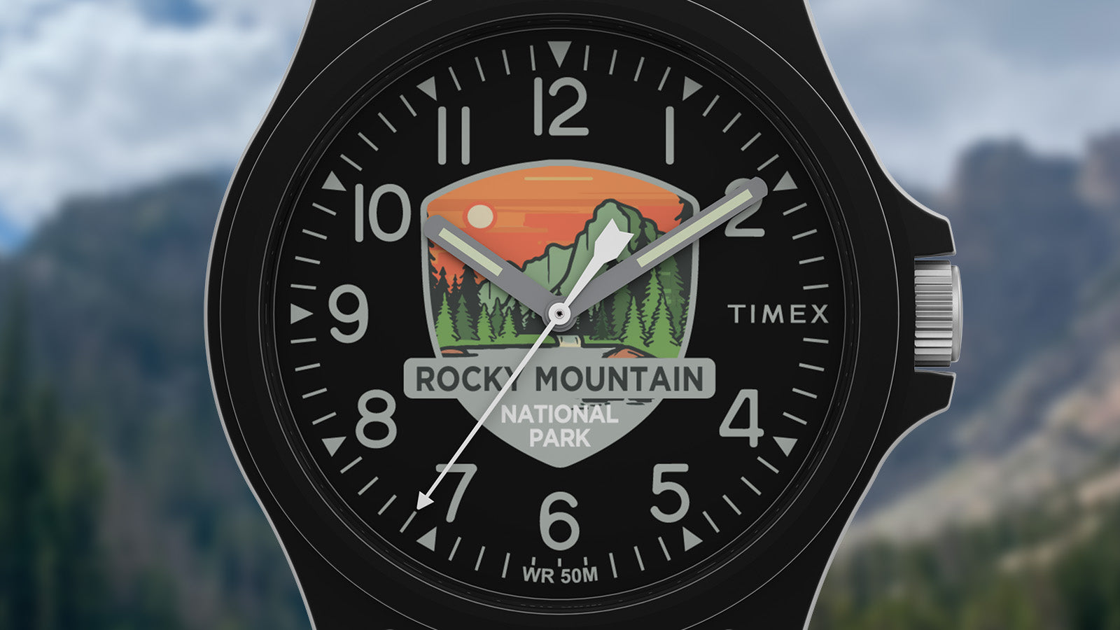 Close-up of the Timex Rocky Mountain National Park watch face with mountain and sunset artwork on a black dial, silver hands, and bold numerals.