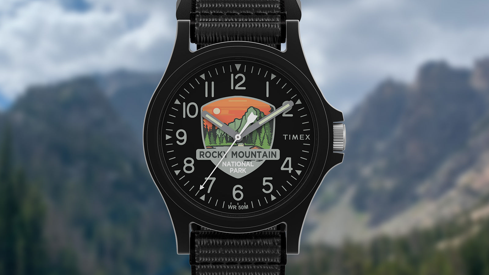 Close-up of the Timex Rocky Mountain National Park watch face with mountain and sunset artwork on a black dial, silver hands, and bold numerals.