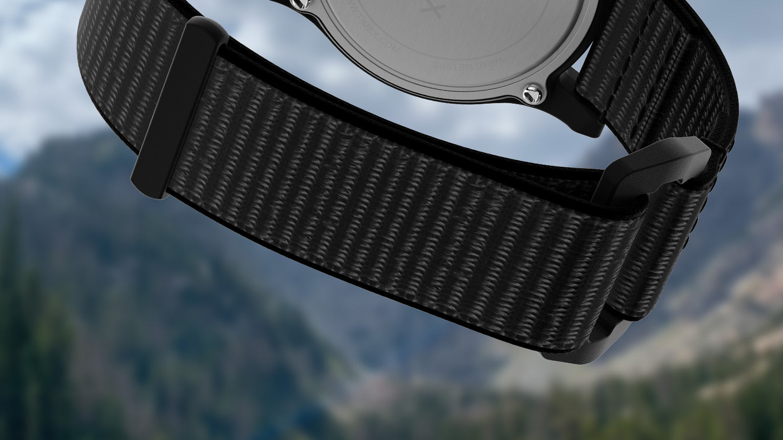 Close-up of the black woven nylon strap of the Timex Rocky Mountain National Park watch, shown against a softly blurred view of the Rocky Mountain peaks.