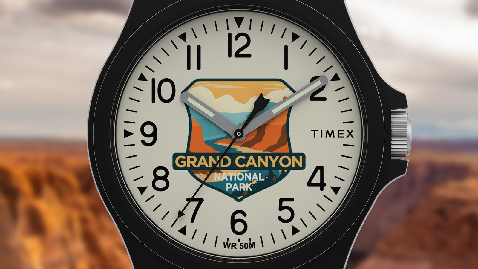 Close-up of the Timex Grand Canyon National Park watch face with desert canyon artwork in orange and blue tones, bold numerals, and luminous hands.