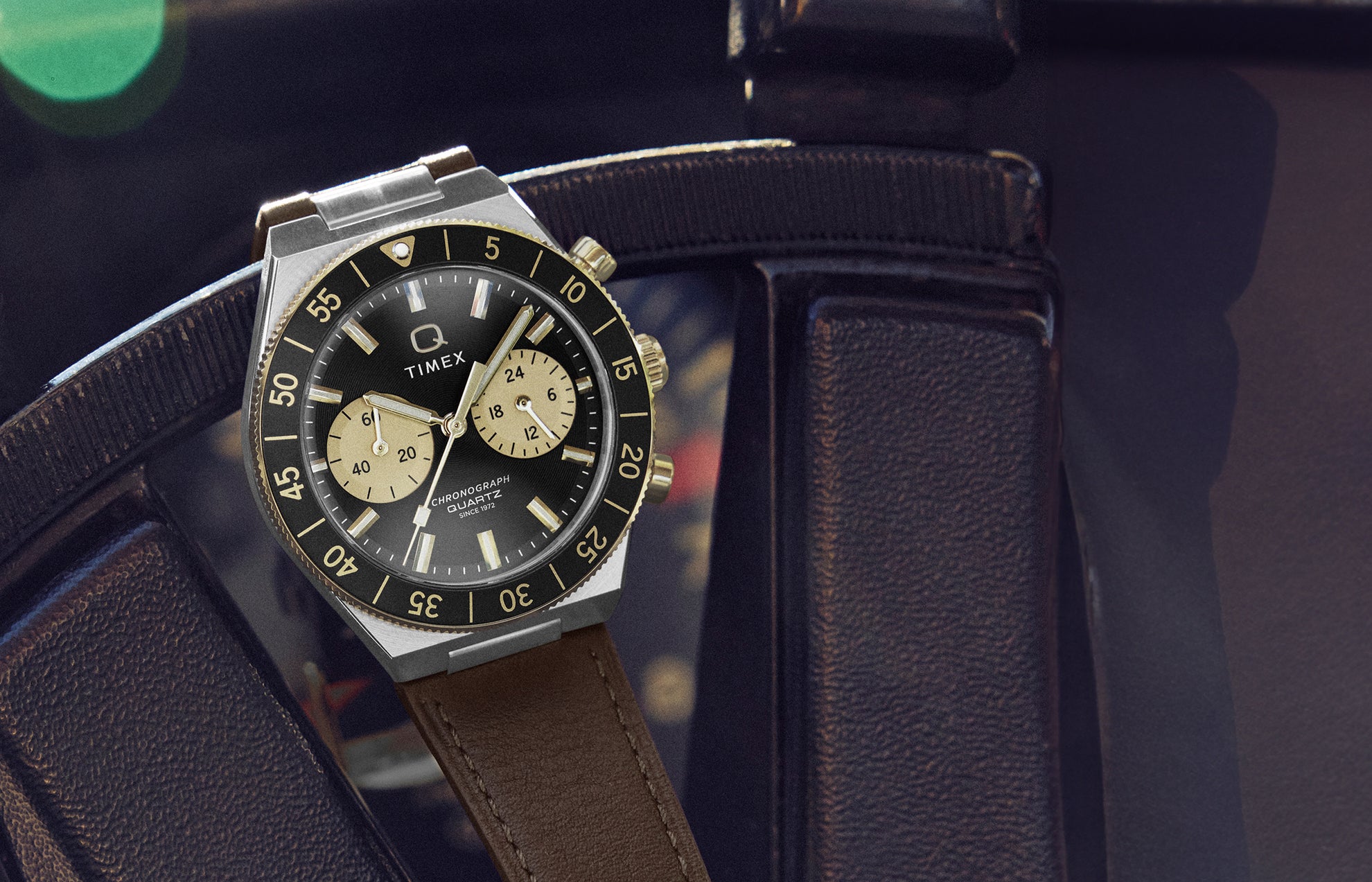 Q Timex® Continental Chronograph watch resting on a vintage car steering wheel, featuring a black dial with champagne subdials and brown leather strap.