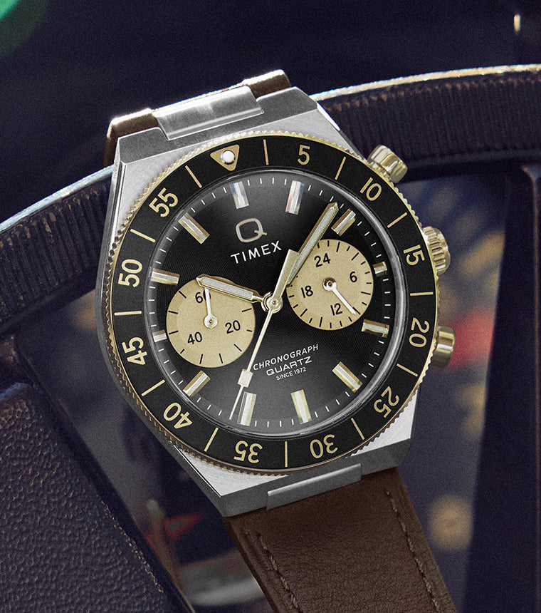 Q Timex® Continental Chronograph watch resting on a vintage car steering wheel, featuring a black dial with champagne subdials and brown leather strap.