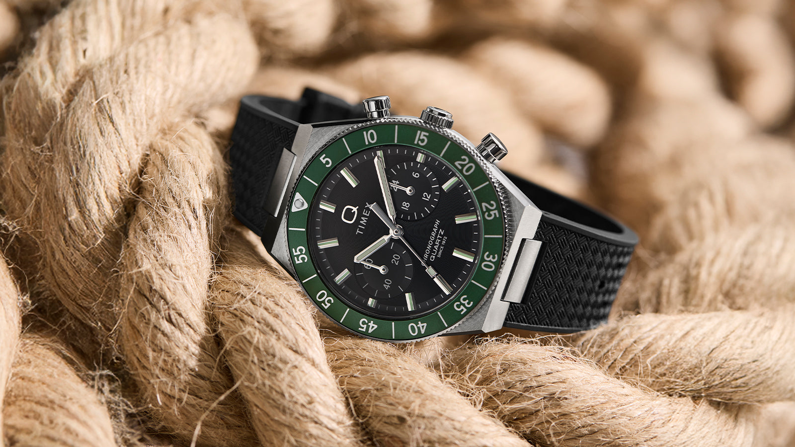 Angled view of the Q Timex® Continental Chronograph with green bezel and black rubber strap, styled on rope.