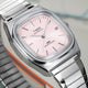 Close-up of the Timex® Automatic 1983 E Line watch showing a light pink sunray dial, applied silver hour markers, date window, and brushed stainless steel case.
