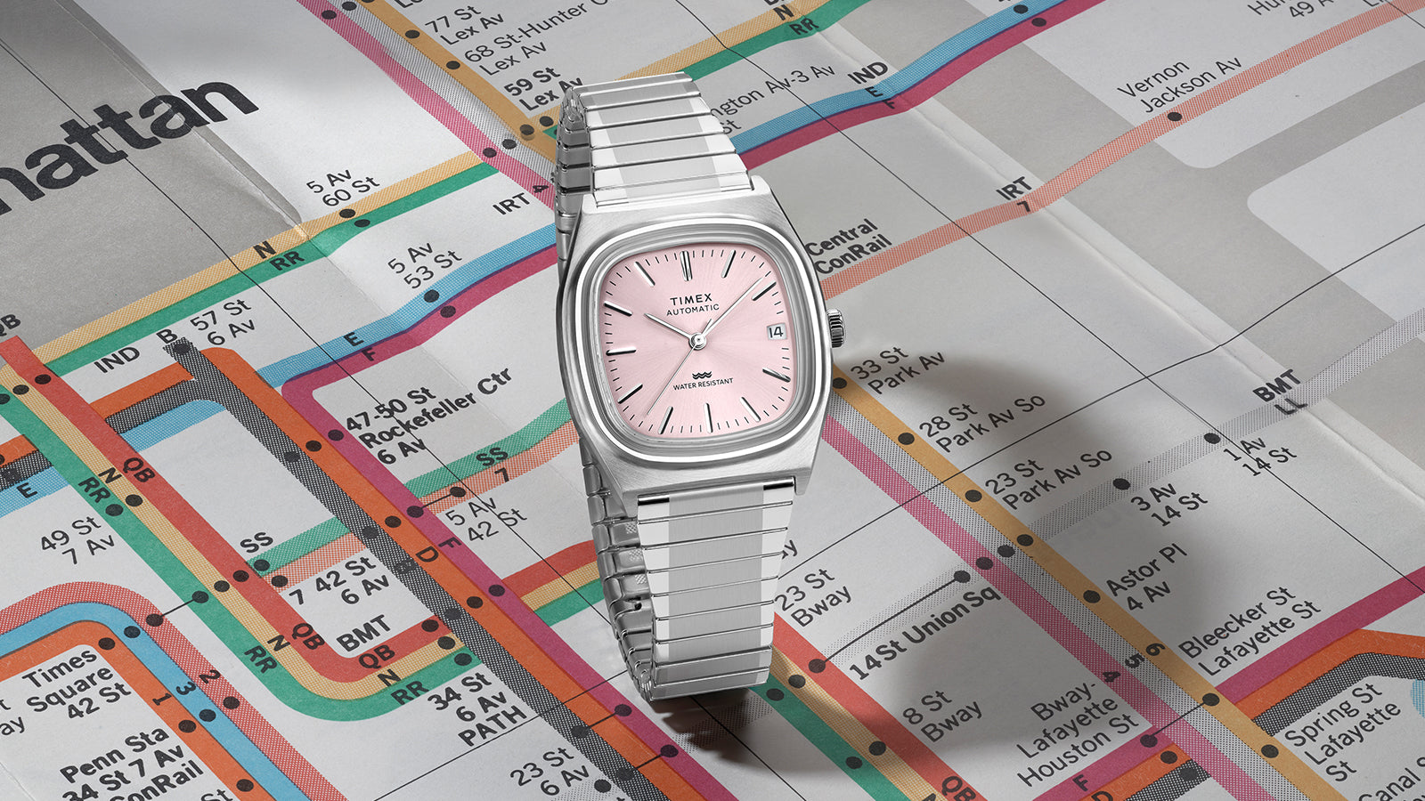 Timex® Automatic 1983 E Line watch with light pink dial and stainless steel expansion bracelet centered on a vintage subway map.