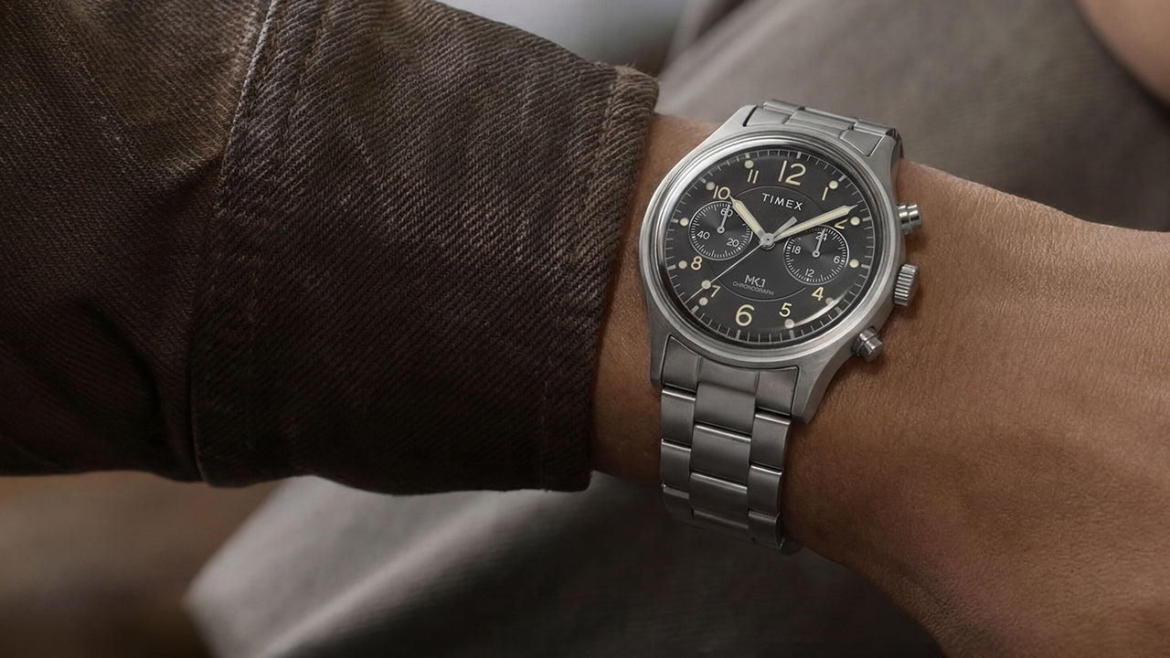 Timex MK1 Chronograph stainless steel watch on wrist with black dial, luminous Arabic numerals, and brushed metal bracelet.