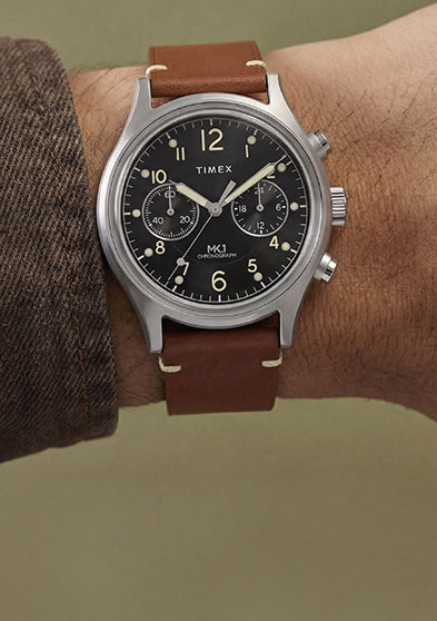 Side view of Timex MK1 Chronograph on wrist with brown leather strap and black dial with luminous Arabic numerals.