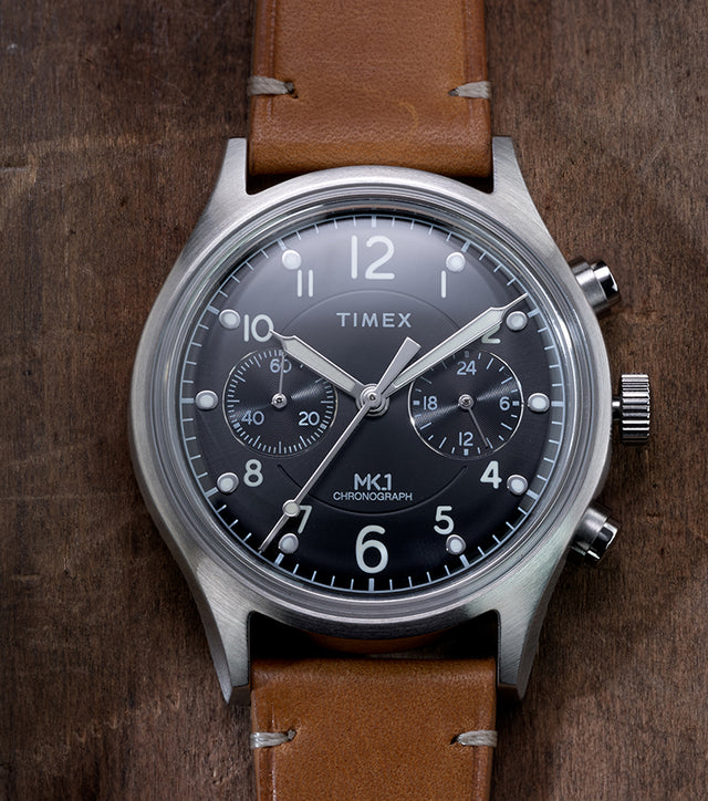 Timex MK1 Chronograph with brown leather strap and black dial, displayed flat on a rustic wooden surface.